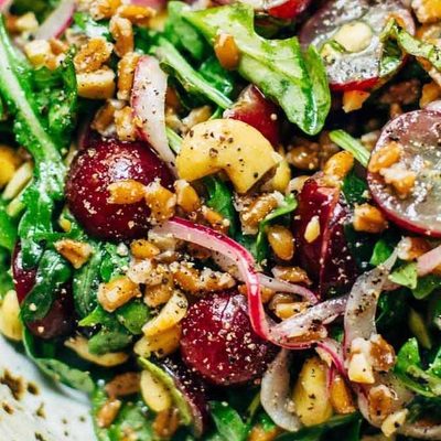 Arugula Salad with grapes, cashews, and pickled red onions in a bowl with a fork.