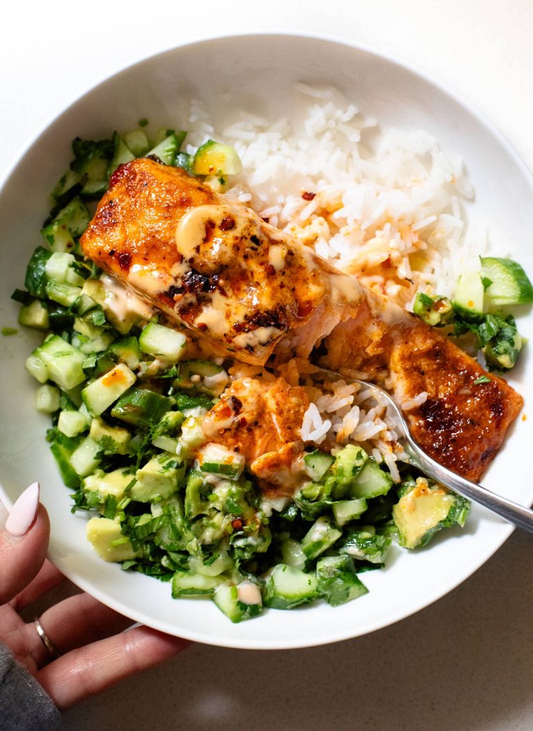 Bang bang salmon in a bowl with rice and cucumber.