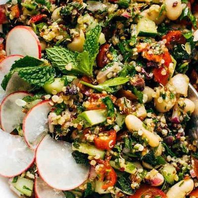 A mixture of quinoa, mint, tomatoes, white beans and radish slices in a bowl.