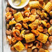 Shrimp, potato and corn mixture on a sheet pan with a side of melted butter in a bowl.