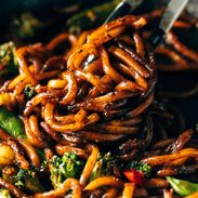 Udon Noodles mixed with fried vegetables and some black pepper in a cooking pan.